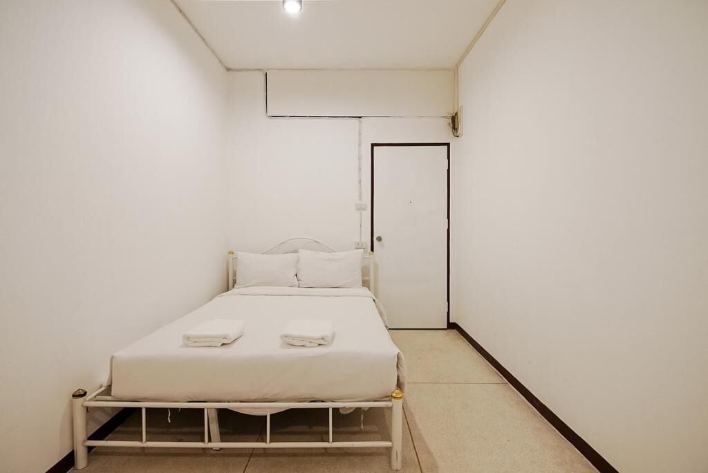 A small, clean room with a single bed, a door, and a light fixture on the ceiling.