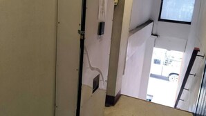 A narrow hallway with a white refrigerator, a window with a view of a vehicle outside, and a ceiling fan. - GO INN Asiatique (Bangkok)