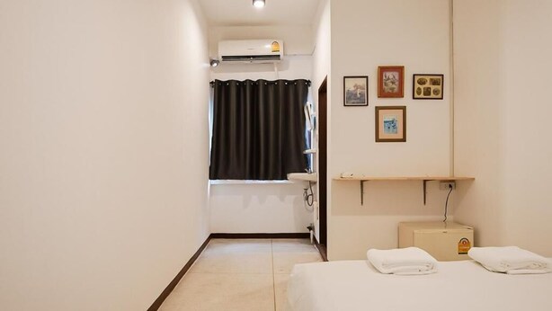 A hotel room with a bed, a bathroom with a shower curtain, a sink, and a wall-mounted shelf with towels. - GO INN Asiatique (Bangkok)