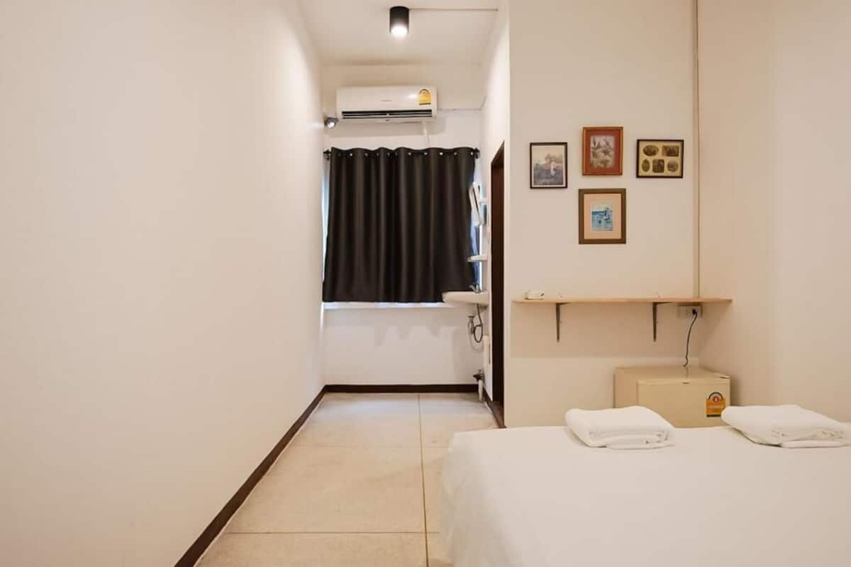 A hotel room with a bed, a bathroom with a shower curtain, a sink, and a wall-mounted shelf with towels.