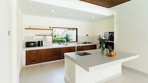 A modern kitchen with a central island, wooden cabinets, a built-in oven, and a large window. - Luxury Noah Villa (Kuta)