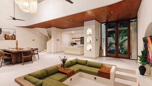 A modern interior with a green sectional sofa, wooden dining table, and ceiling fans. - Luxury Noah Villa (Kuta)