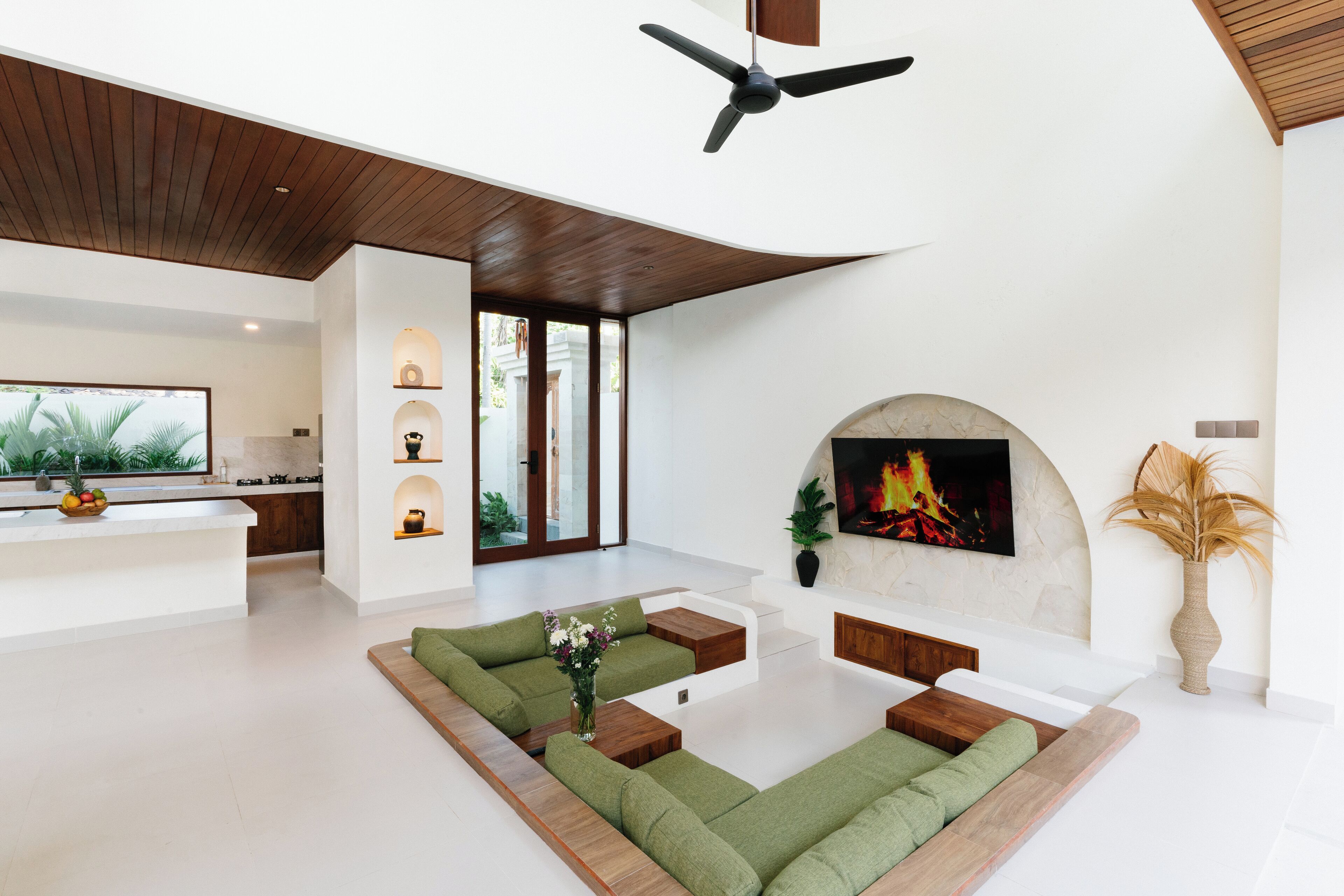 A modern living room with a fireplace, green sofas, and a flat-screen TV.