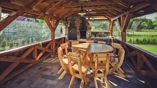 Een terras van hout met een stenen open haard, een ronde houten tafel en houten stoelen.