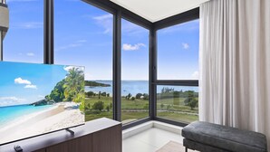 A modern room with large windows, a flat-screen TV, a dark-toned sofa, and a minimalist design. - B-701 Stunning corner ocean view (Cupecoy)