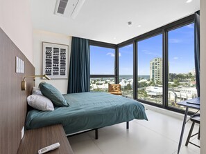A modern bedroom with a large bed, a desk, and a view of the city. - B-701 Stunning corner ocean view (Cupecoy)