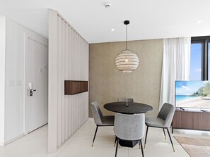 A modern dining area with a round table, two grey chairs, a pendant light, and a television on a wooden cabinet. - B-701 Stunning corner ocean view (Cupecoy)