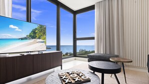 A modern living room with a large TV, two round tables, and a view of a beach. - B-701 Stunning corner ocean view (Cupecoy)