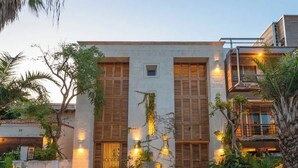 A modern building with a brick pathway leading to a gated entrance, surrounded by greenery and illuminated by wall-mounted lights.