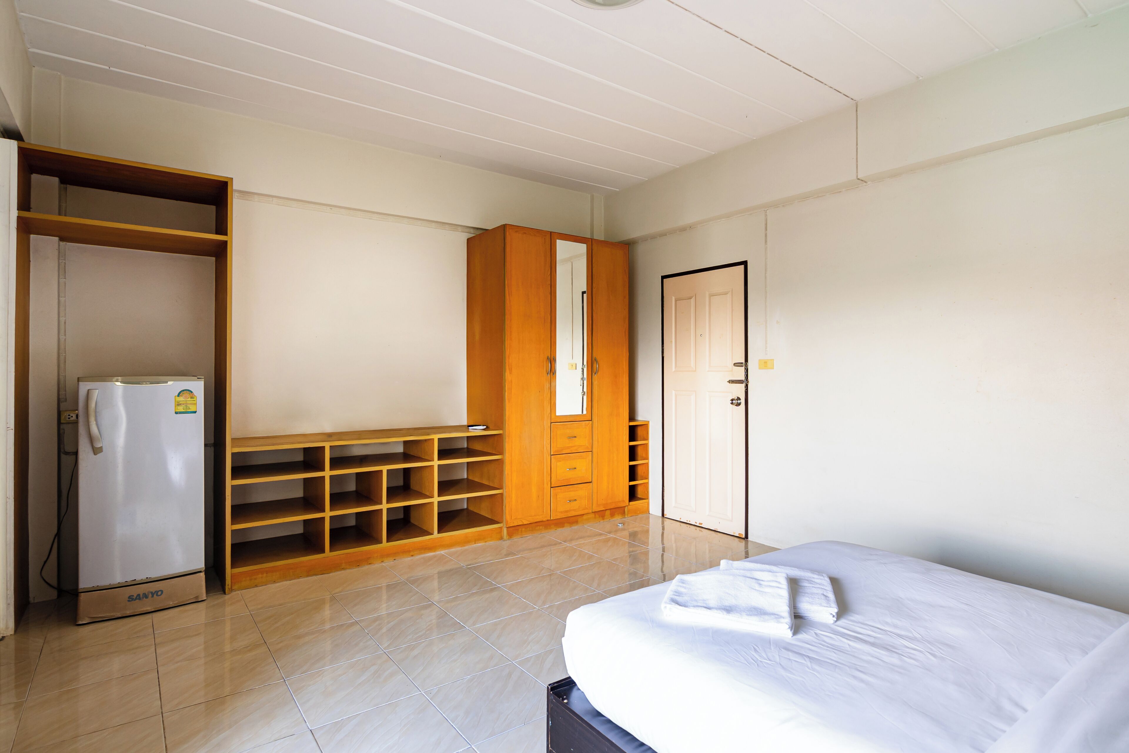 A room with a bed, a wardrobe, a mirror, and a refrigerator.