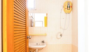 Une salle de bain avec une porte en bois, un lavabo blanc, une douchette jaune et un miroir.