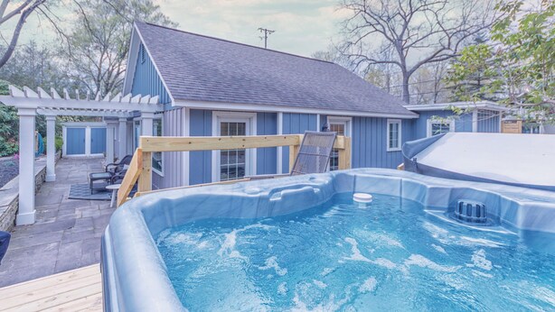 Ein Garten mit Whirlpool, einer Pergola und einem Haus mit blauer Fassade.