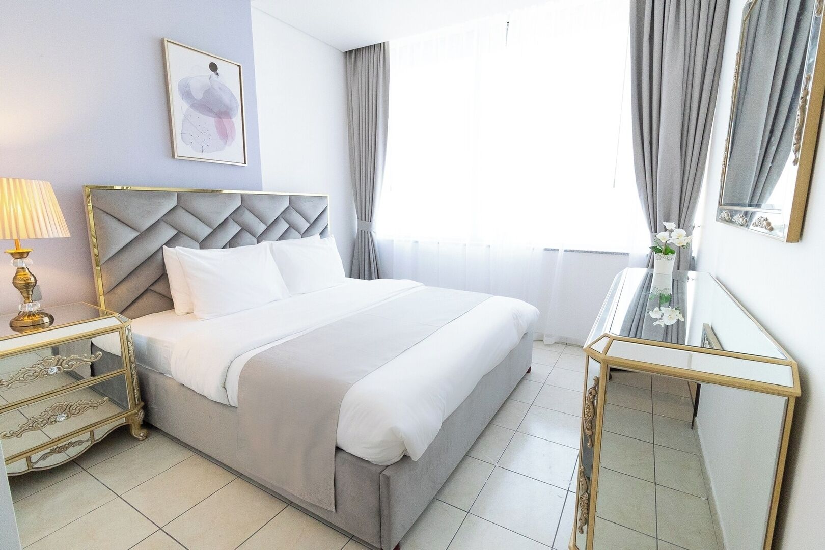 A hotel room with a large bed, a bedside table with a lamp, a mirror, and a framed picture on the wall.