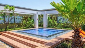 Une piscine rectangulaire à l’eau d’un bleu limpide, entourée d’escaliers en bois et d’une végétation luxuriante, notamment des palmiers et divers arbustes.