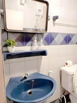 Un baño con un lavabo azul, un espejo, un inodoro y un estante con artículos de aseo.