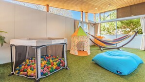 Zona de juegos con piscina de pelotas, una pequeña tienda de campaña, una hamaca y un sillón de peluche azul.