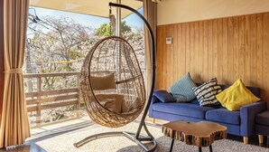 Una habitación con una silla colgante, un sofá azul con cojines, una mesa de madera y vistas a flores de cerezo.