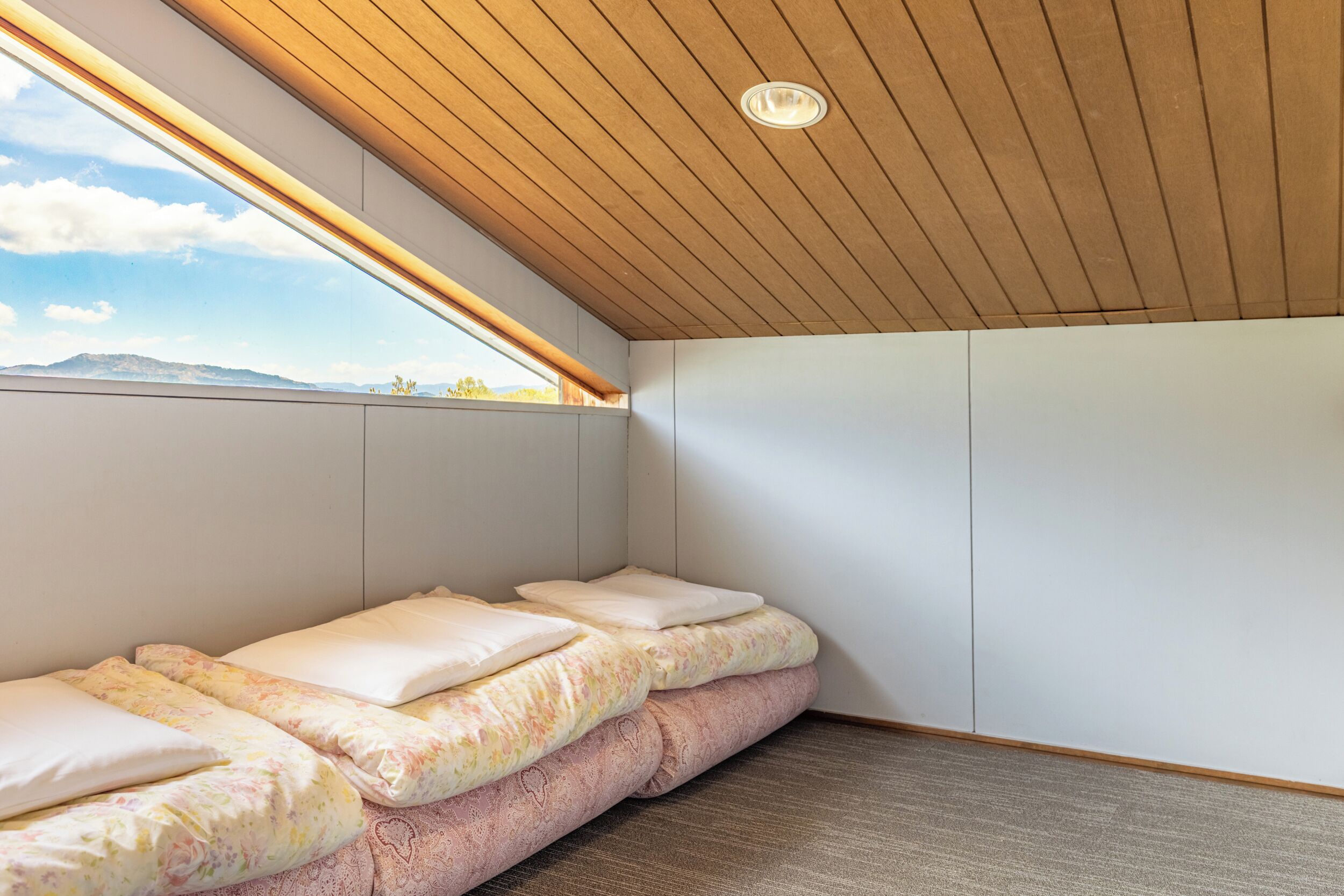 A room with a sloped ceiling, a bed with floral bedding, and a view of the outdoors.