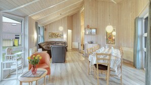 A spacious living area with a high ceiling, wooden walls, a dining table set for six, and a comfortable seating area with a sofa and chairs. - 4 Star Holiday Home in Ottendorf (Otterndorf)