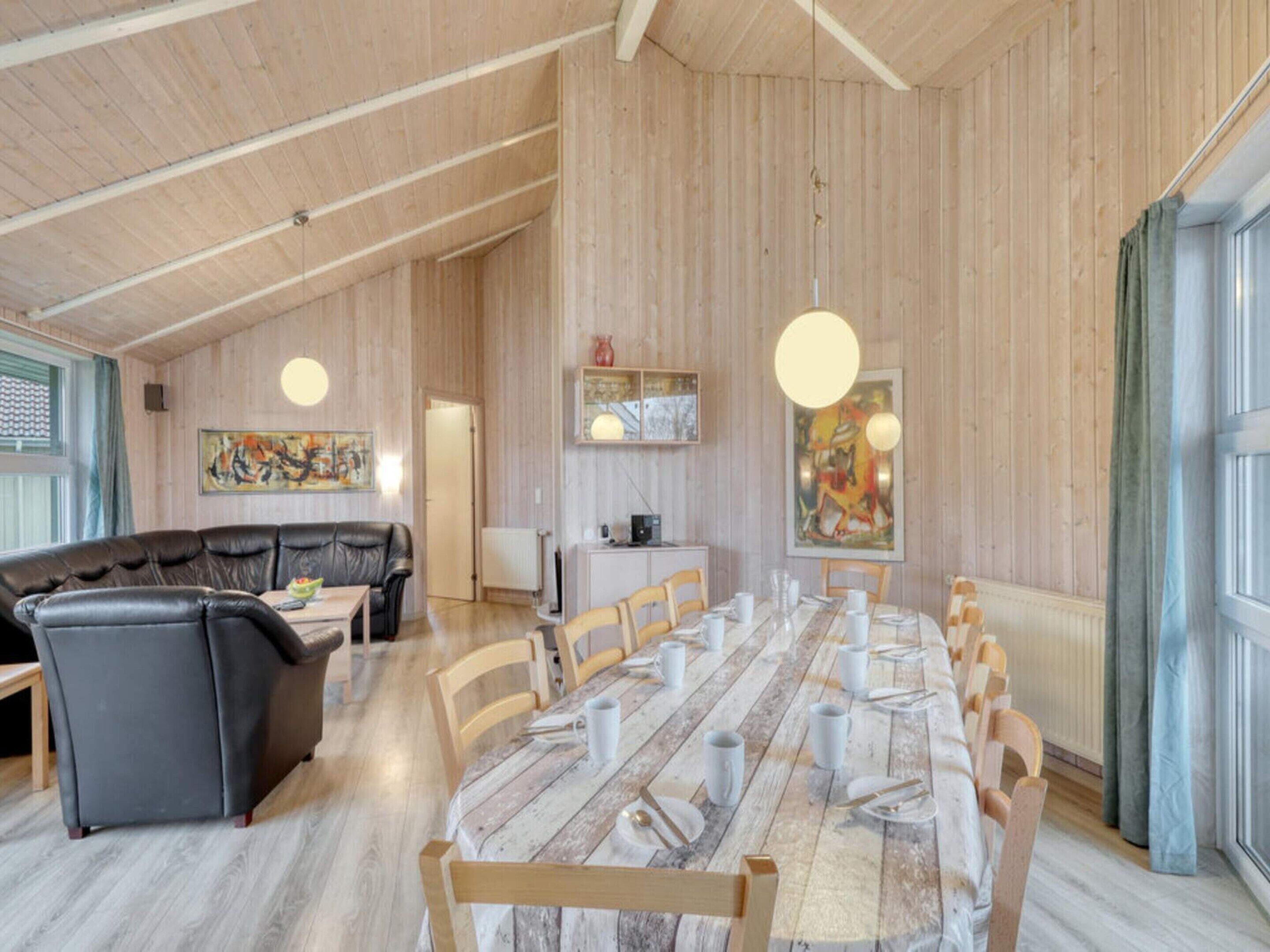 Un comedor amplio con una larga mesa de madera dispuesta para una comida, rodeado de sillas de madera.