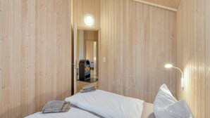 A wooden cabin room with a bed, a reading light, and a fireplace. - 4 Star Holiday Home in Ottendorf (Otterndorf)