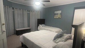 Ein Schlafzimmer mit zwei Betten, einem Deckenventilator, einem Nachttisch und einer Wandlampe.