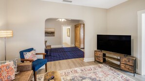 A living room with a TV, a blue armchair, a patterned rug, and a wooden cabinet. - Chic & Cozy 3BR 2BA Home - Heart of GNV! (Gainesville)