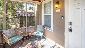 A covered porch with wicker chairs and a small table, a white door with a keypad lock, and a street sign with the number 702. - Chic & Cozy 3BR 2BA Home - Heart of GNV! (Gainesville)