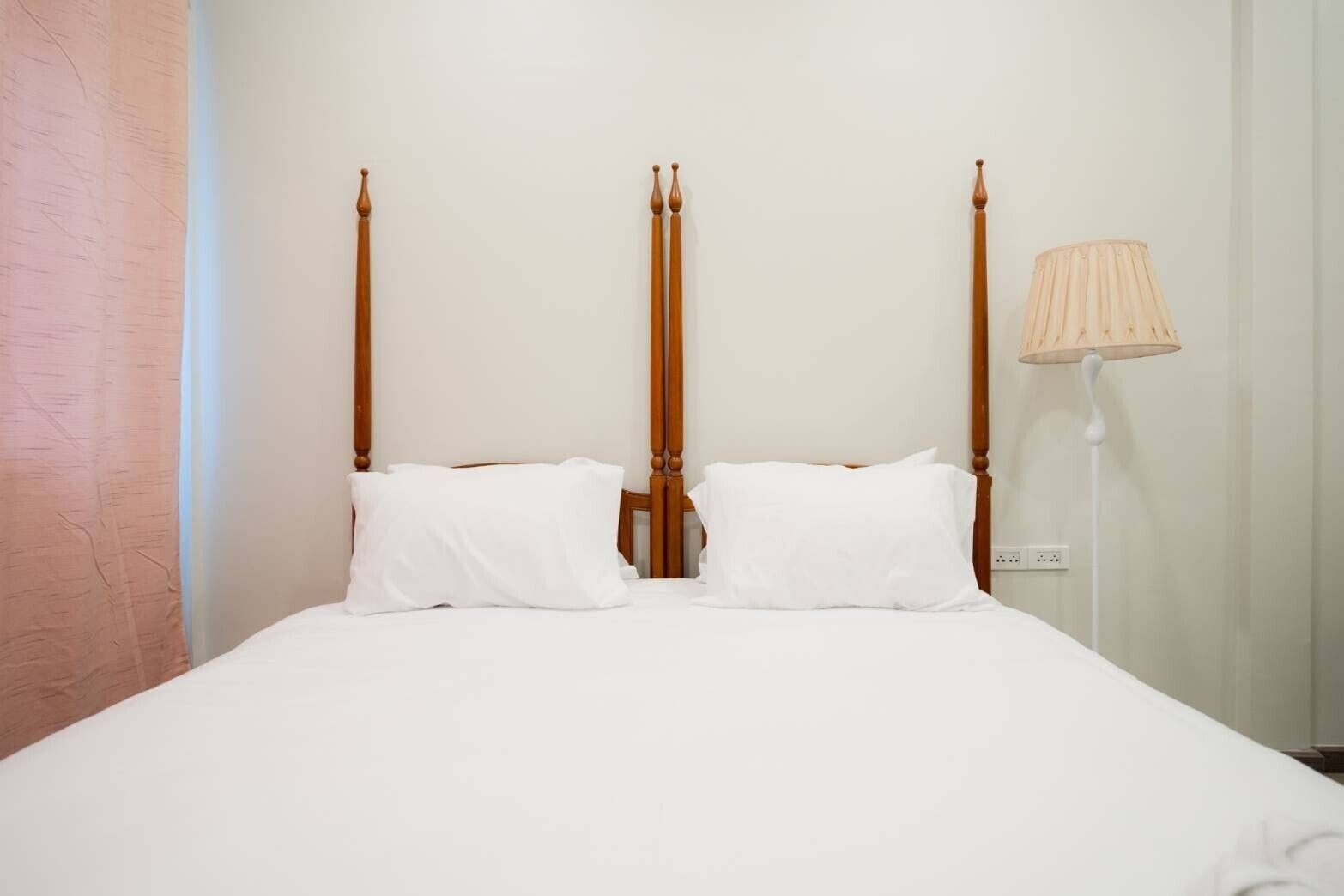 Una cama con cabecera de madera, dos almohadas blancas y una lámpara de noche.