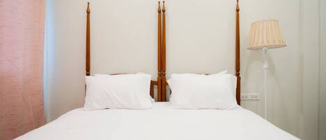 Una cama con cabecera de madera, dos almohadas blancas y una lámpara de noche.