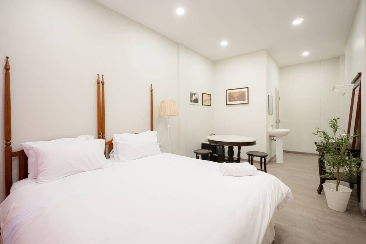 Een hotelkamer met een groot bed, een ronde tafel met twee stoelen, een klein wastafeltje en een potplant.