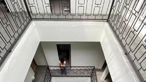A multi-level atrium with a central open space, a staircase, and a person standing on an upper level. - CASA Yaowarat (Bangkok)