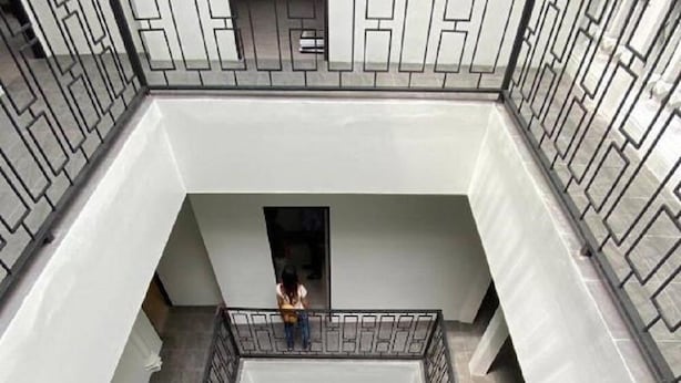 A multi-level atrium with a central open space, a staircase, and a person standing on an upper level. - CASA Yaowarat (Bangkok)