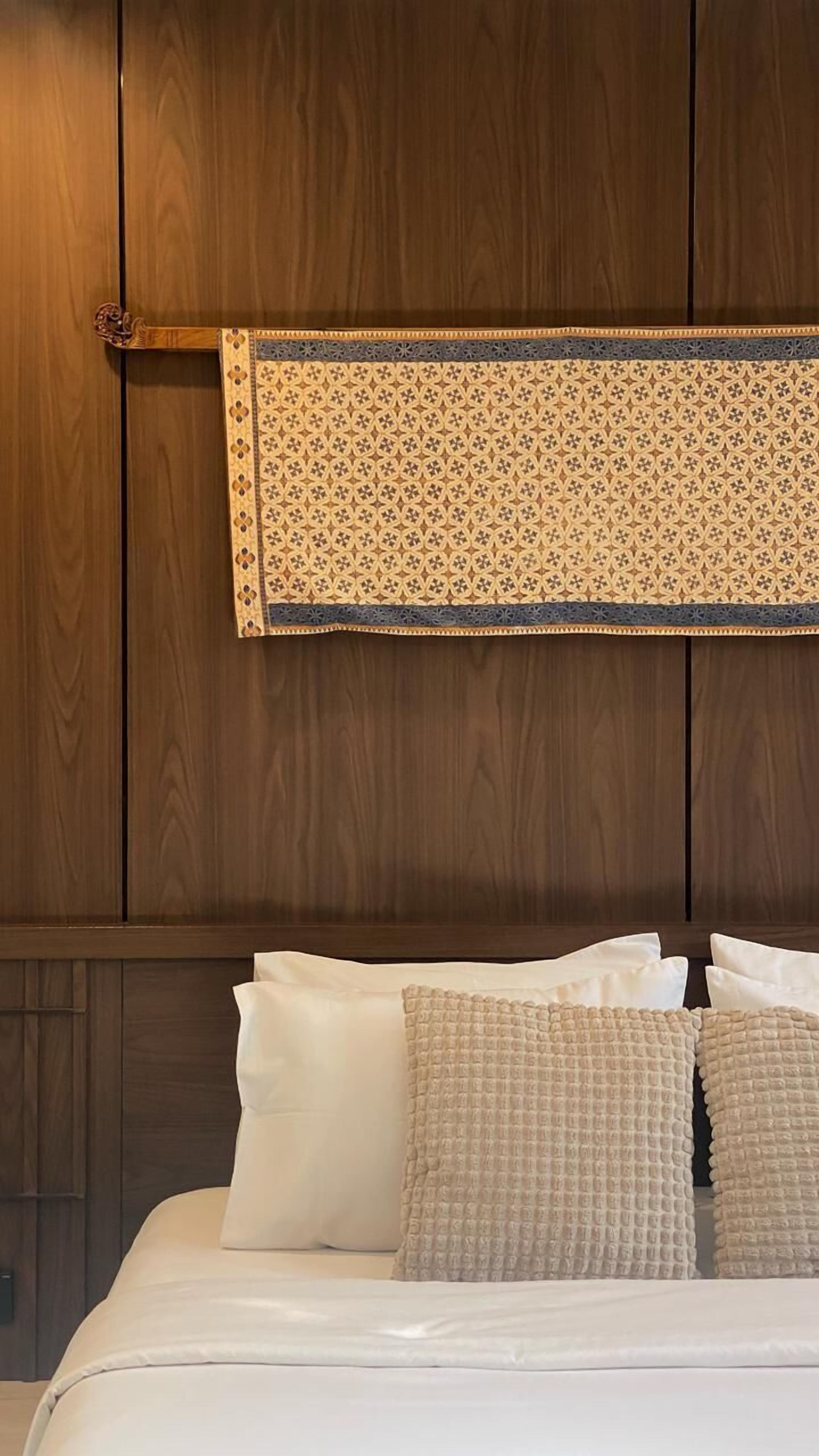 A bed with white bedding and two beige pillows, a wooden headboard, and a decorative wall hanging above the bed.