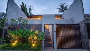 Una casa moderna con una escalera central, un acceso con portón y un jardín bien cuidado.