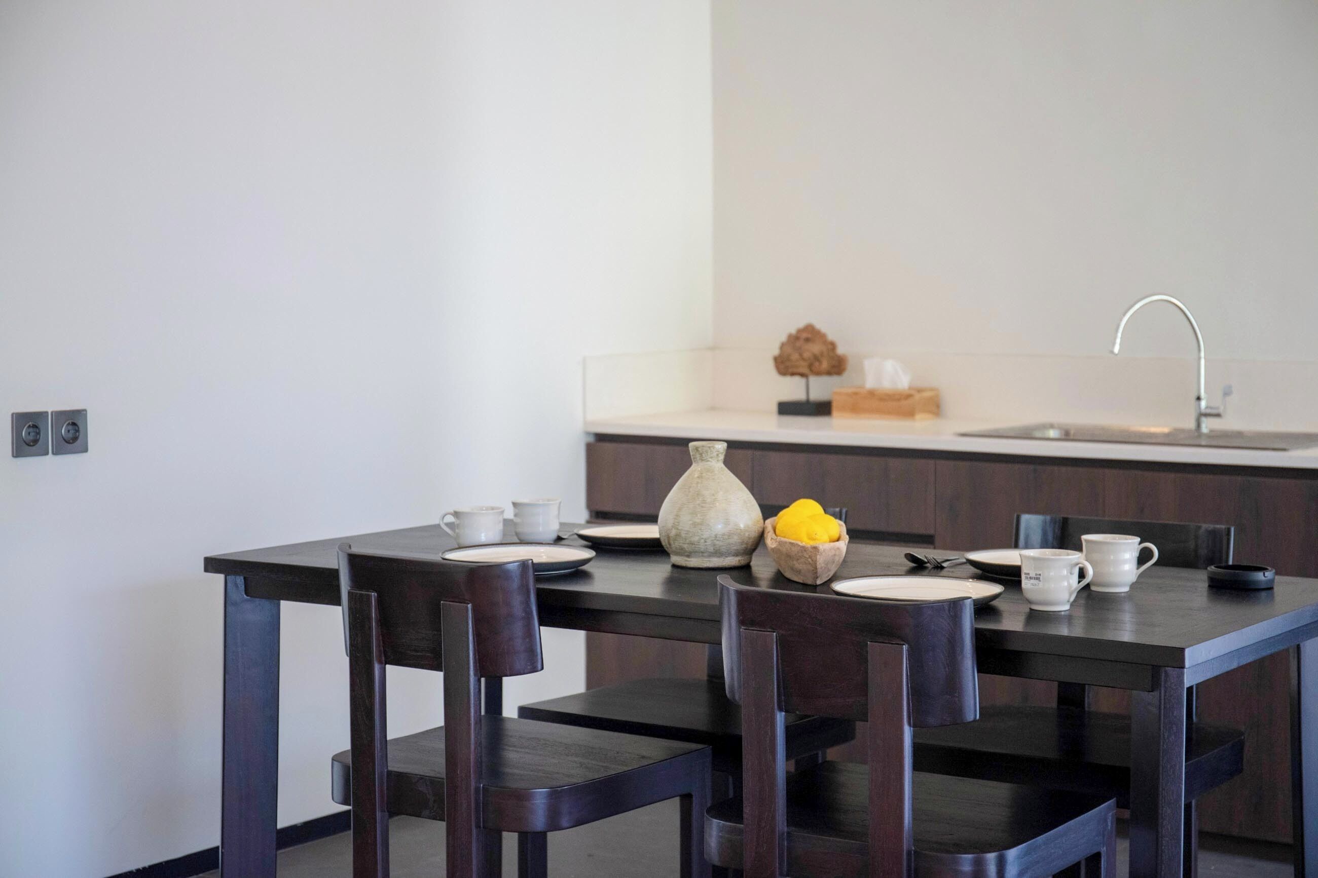 A dining table with chairs, a vase, and a bowl of lemons.