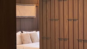Un dormitorio moderno con un armario de madera, una cama con ropa de cama blanca y una mesita con un objeto amarillo.