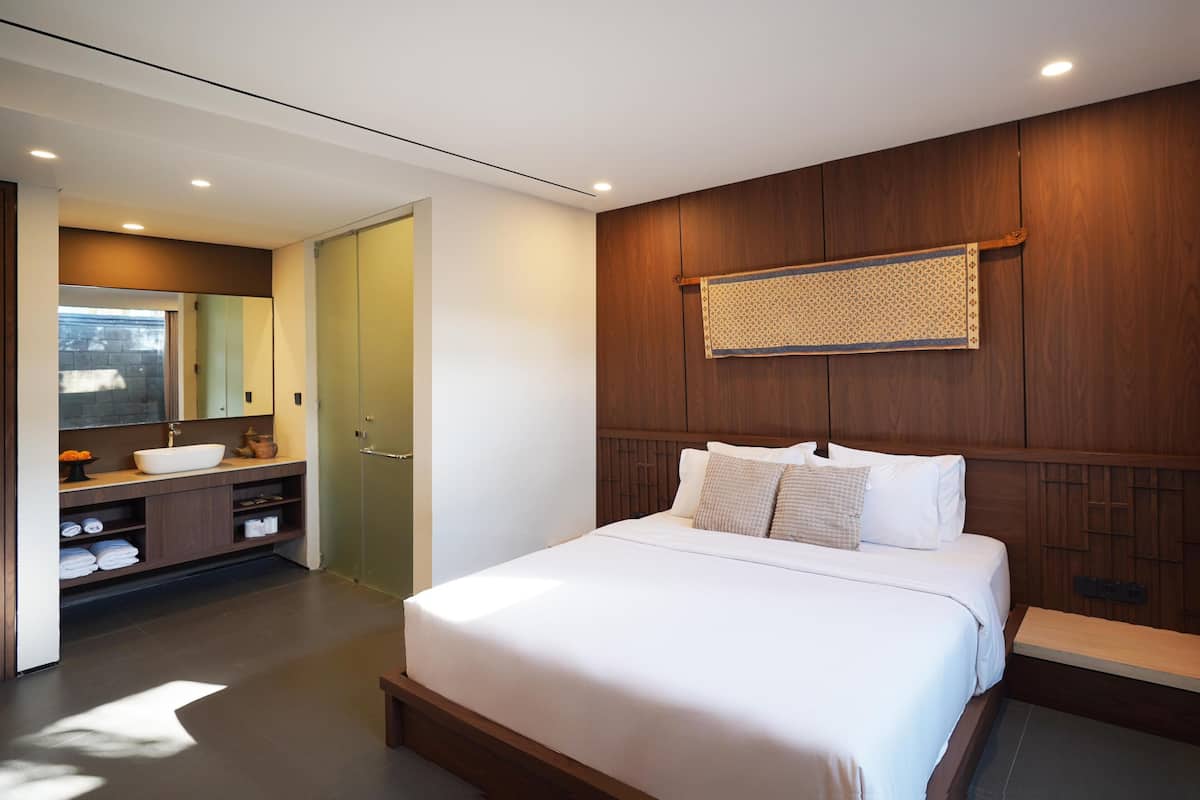A modern bedroom with a large bed, wooden paneling on the walls, a vanity with a mirror, and a small window.