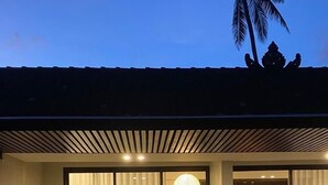 Un dormitorio moderno con una cama grande, una mesita con botellas y vistas a un edificio tradicional y una palmera.