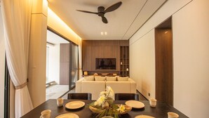 Un comedor moderno con una mesa oscura dispuesta para cuatro, un ventilador de techo y un sofá al fondo.