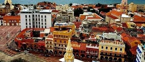 An aerial view of a historic city with a prominent church featuring a tall bell tower, surrounded by colorful buildings and a large open square.