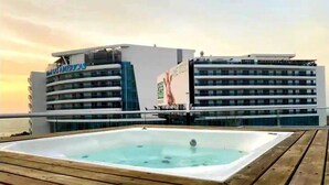 A pool area with a wooden deck, a hot tub, and a view of a hotel building with multiple floors and balconies. - Apt close to the Sea, Historic Center and Las Americas. (Cartagena)