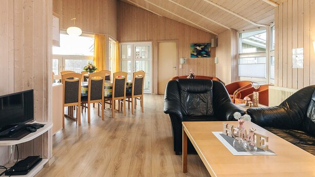 A spacious living area with a wooden floor, a dining table with chairs, a leather sofa, and a television on a stand. - 4 Star Holiday Home in Ottendorf (Otterndorf)