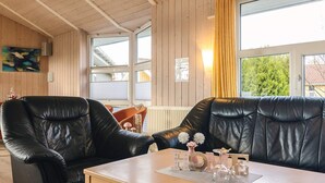 A cozy room with a black leather sofa and a wooden table, large windows with yellow curtains, and a wooden ceiling. - 4 Star Holiday Home in Ottendorf (Otterndorf)