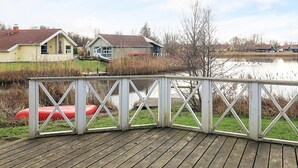 A wooden deck with a white railing overlooking a calm lake, surrounded by houses and vegetation. - 4 Star Holiday Home in Ottendorf (Otterndorf)