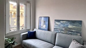 Un salon avec un canapé gris, une plante en pot et deux tableaux accrochés au mur.