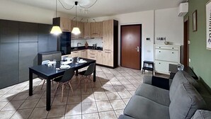 Uma cozinha moderna com armários escuros, uma mesa de jantar posta para quatro pessoas e um sofá cinza na sala de estar.