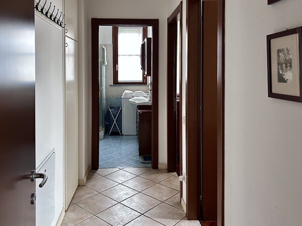 A hallway leading to a bathroom with a window, a drying rack, and a framed picture on the wall.