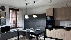 Cozinha moderna com área de refeições, destacando uma mesa preta, cadeiras e luminárias pendentes.
