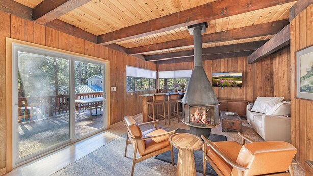 A cozy cabin interior with a fireplace, wooden furniture, and large windows offering a view of the outdoors. - Central 3 Bedroom House Less Than a Mile to Heavenly (South Lake Tahoe)